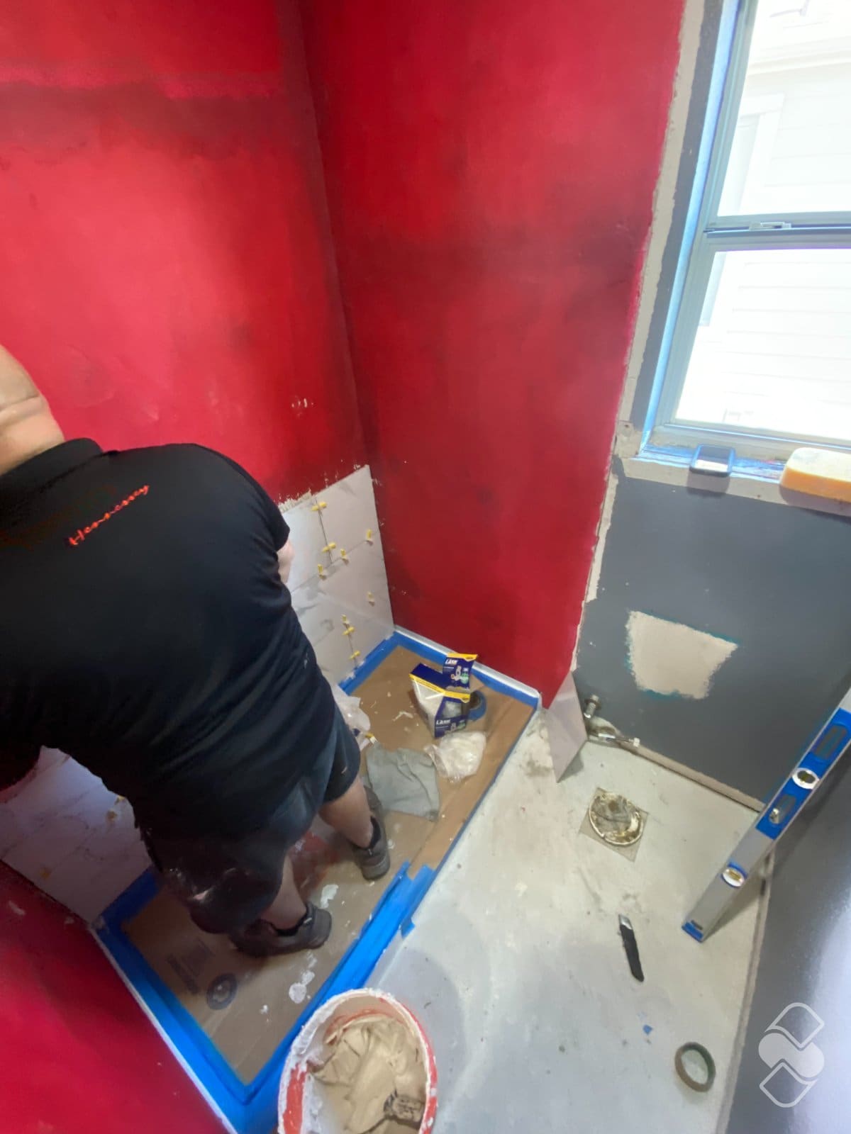 Shower walls coated in red waterproofing membrane while the first rows of white tile are set over the protected pan