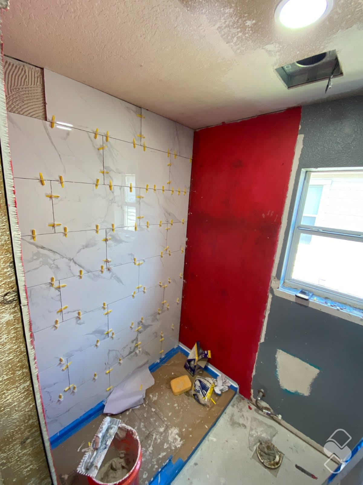 Marble look porcelain tile with spacers being set over a red waterproofed shower wall