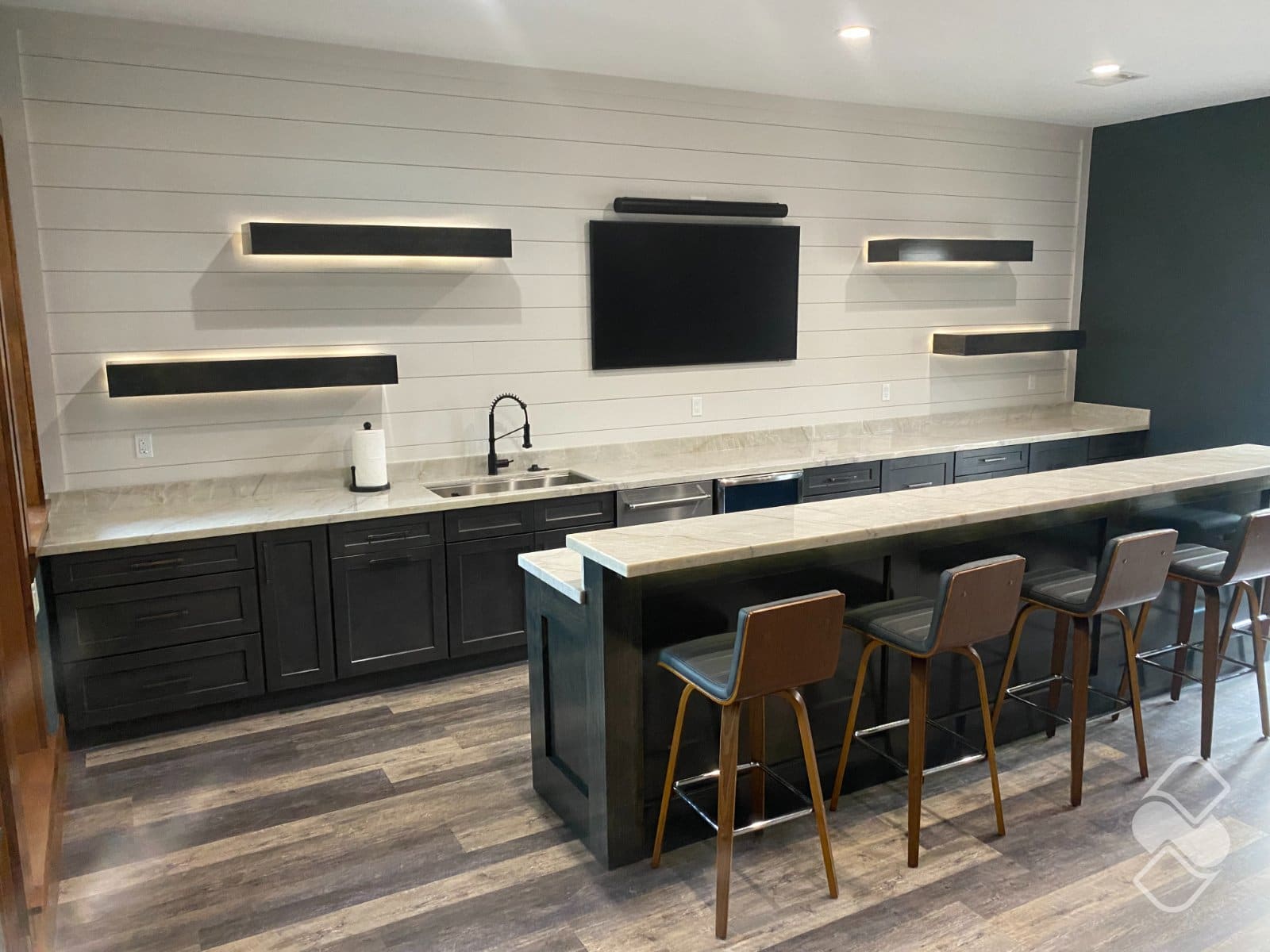 Custom floating wood shelves with warm accent lighting mounted on a white shiplap wall above dark bar cabinetry