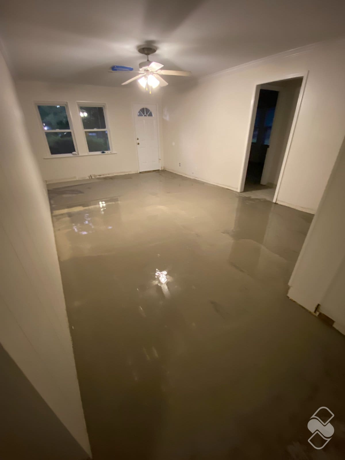 Gray self leveling compound poured across a living room subfloor before plank installation