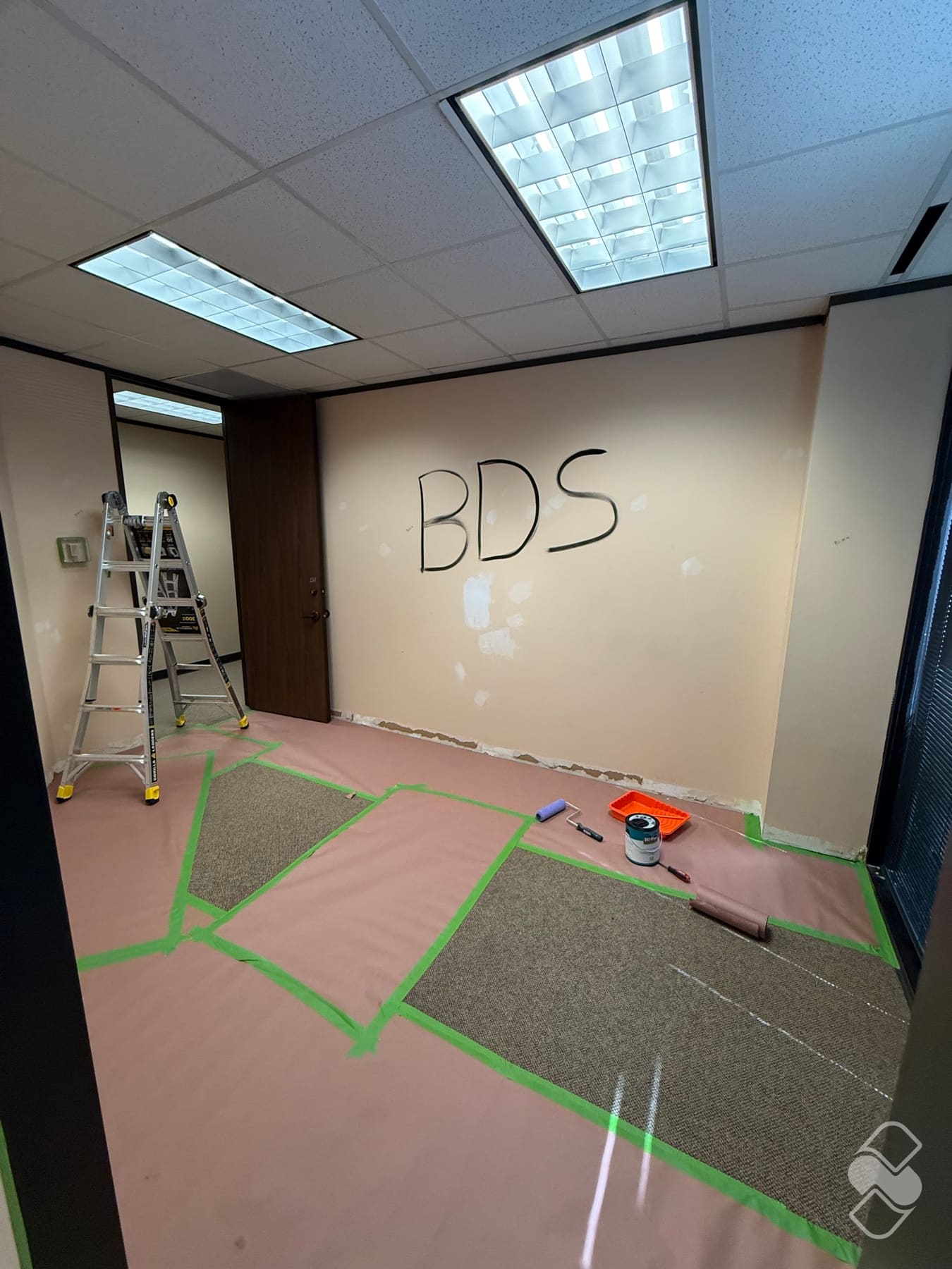 Office suite with floors fully papered and edges taped, the previous tenant's logo still visible on the wall before painting