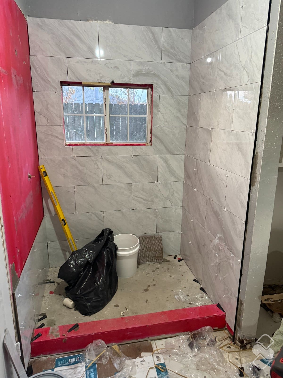Tile shower rebuild with red waterproofing membrane visible on one wall and on the curb beneath new marble look tile