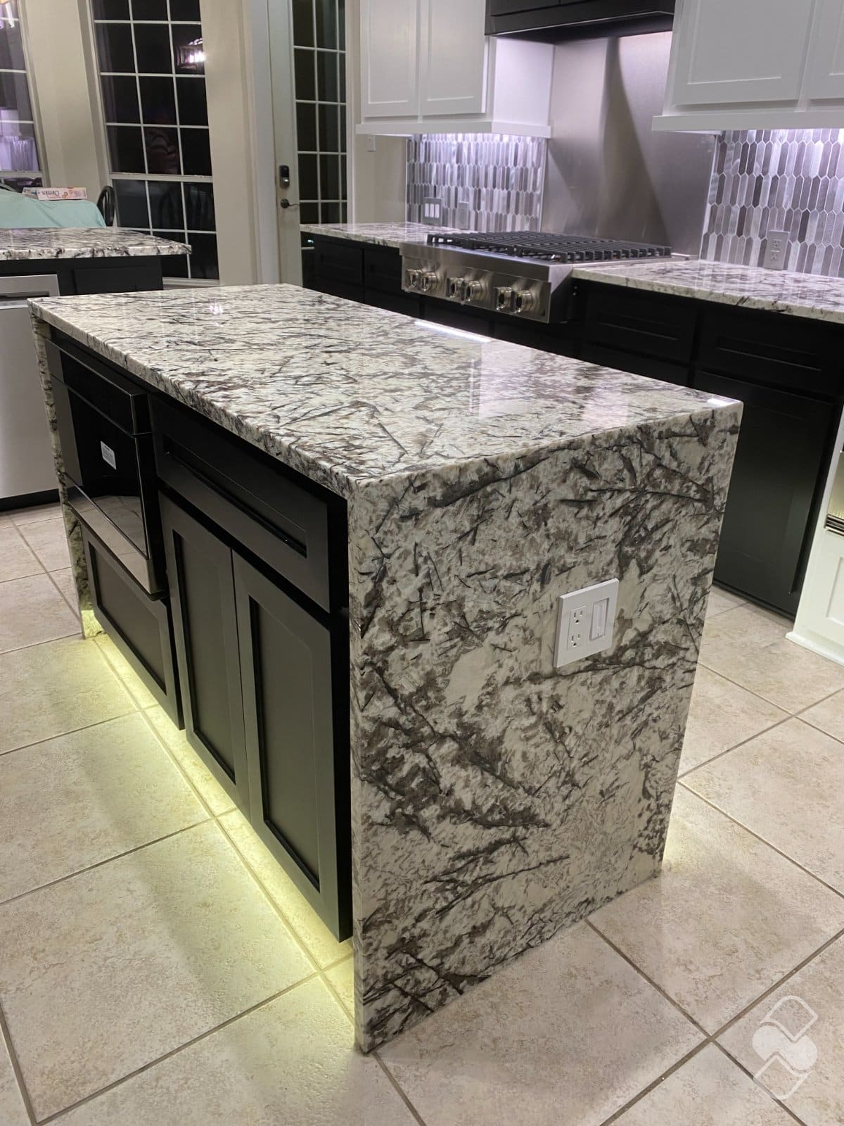 Kitchen island with waterfall edge stone carried down the side of the cabinetry to the floor