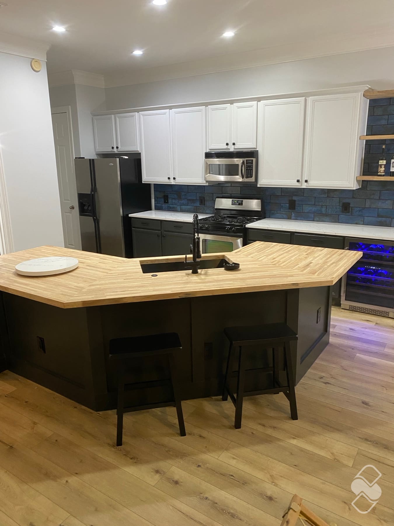 Open kitchen after a full remodel with a custom butcher block island, white upper cabinets, and charcoal base cabinets